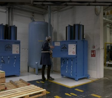 Man i tillverkningsmiljö som öppnar en blå balpress med Mil-tek-logotyp